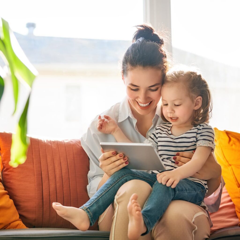 Mother holding child while sitting on a couch looking at tablet